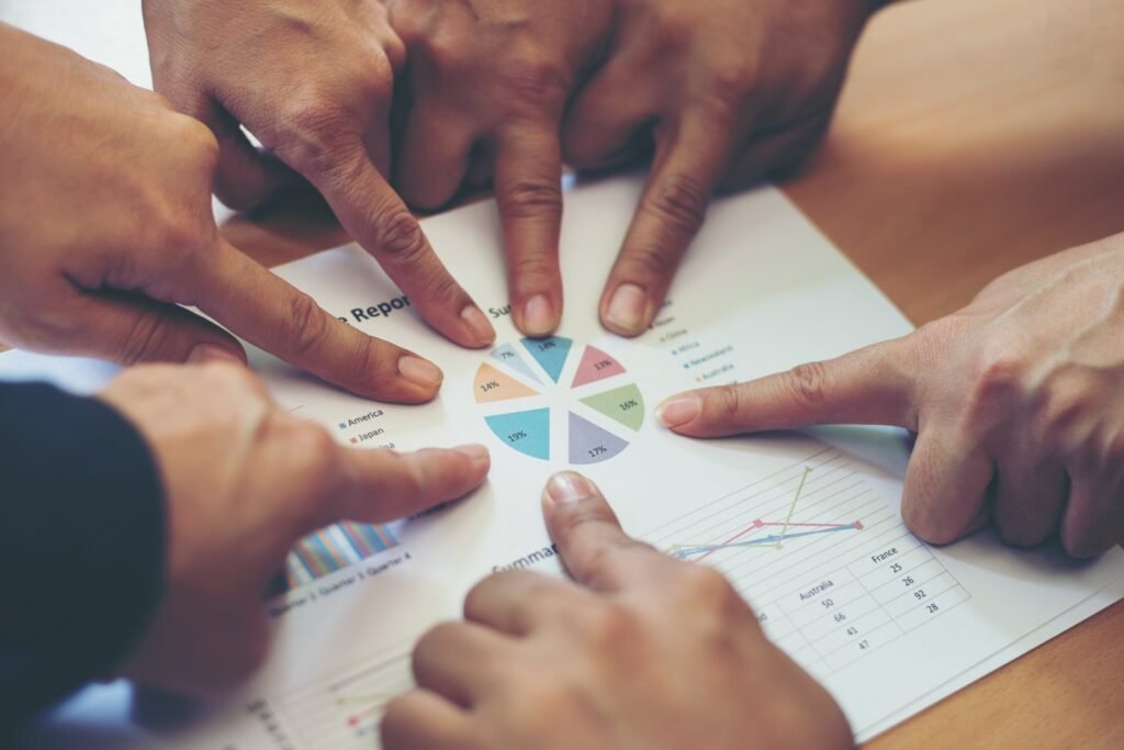 Several hands pointing at a shared chart on a table, representing community collaboration